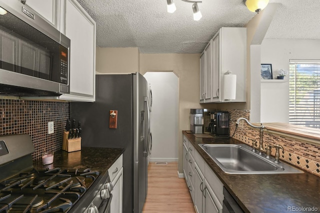 kitchen featuring light wood-style flooring, a sink, appliances with stainless steel finishes, dark countertops, and backsplash