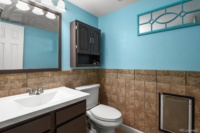 half bath with a wainscoted wall, toilet, tile walls, and vanity