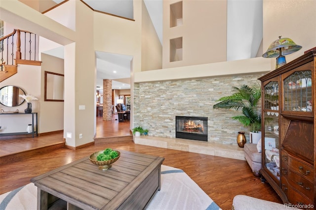 living area with baseboards, a towering ceiling, wood finished floors, stairway, and a fireplace