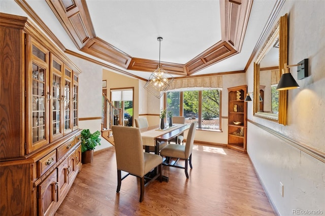 dining room featuring a raised ceiling, ornamental molding, an inviting chandelier, and light wood-style floors