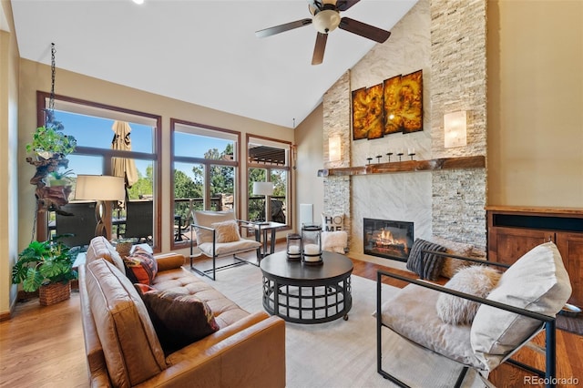 living area featuring a stone fireplace, ceiling fan, high vaulted ceiling, and wood finished floors