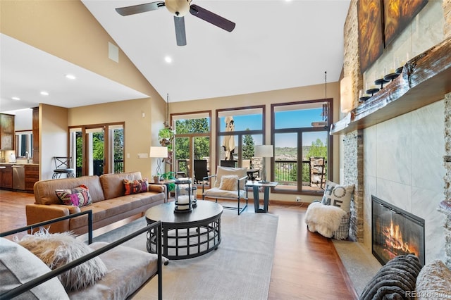 living area with a healthy amount of sunlight, a ceiling fan, high vaulted ceiling, and a tiled fireplace