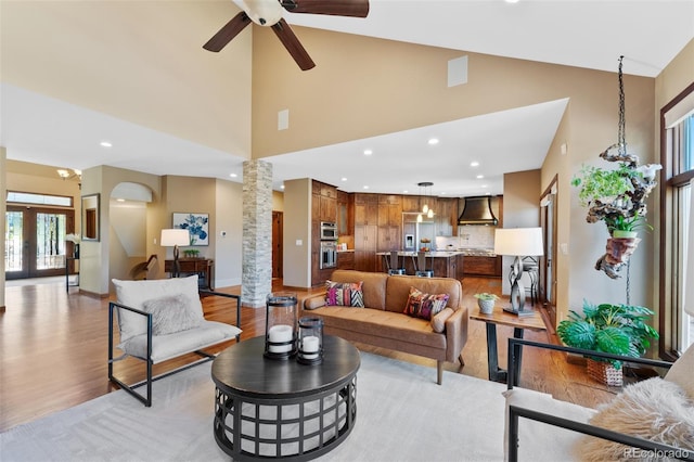 living room with light wood-style floors, high vaulted ceiling, a ceiling fan, and decorative columns