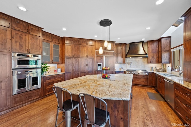 kitchen featuring a sink, stainless steel appliances, a kitchen island, custom range hood, and light wood-style floors