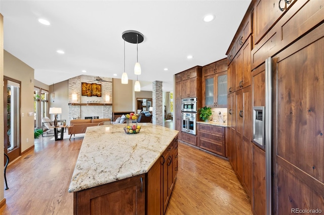 kitchen with paneled built in refrigerator, light wood-type flooring, decorative columns, and a kitchen island