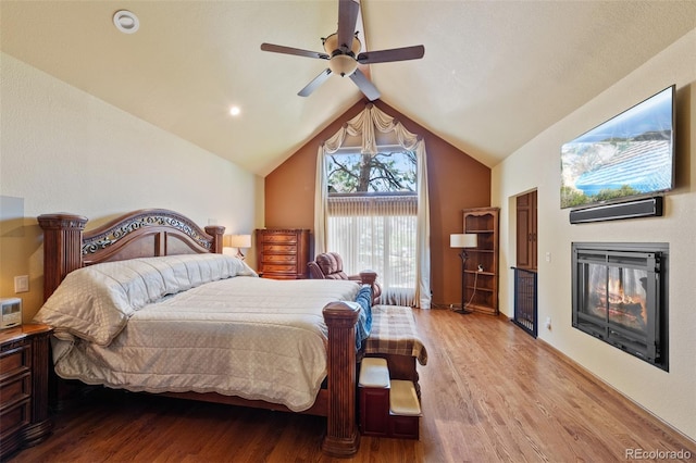 bedroom with vaulted ceiling, wood finished floors, a ceiling fan, and a glass covered fireplace