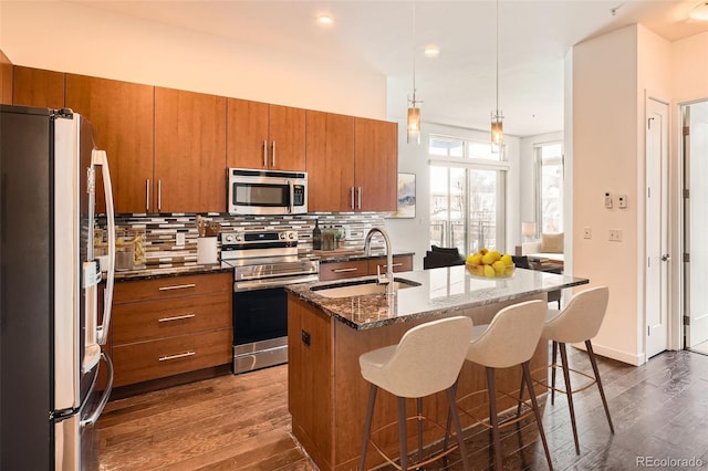 336 E 1st Ave Unit 200, Denver, CO 80203 - kitchen with stainless steel appliances, brown cabinets, dark wood-style flooring, backsplash, and a breakfast bar area