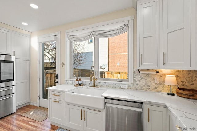 kitchen with sink, white cabinets, dishwasher, and light stone countertops