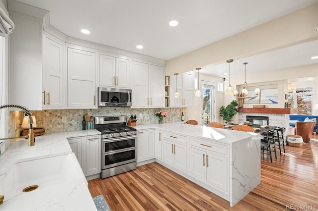 kitchen with light wood-type flooring, decorative backsplash, a peninsula, stainless steel appliances, and a sink
