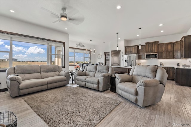 living room featuring ceiling fan with notable chandelier, recessed lighting, and light wood-style floors