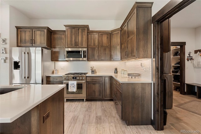 kitchen with light countertops, backsplash, appliances with stainless steel finishes, dark brown cabinets, and light wood-type flooring