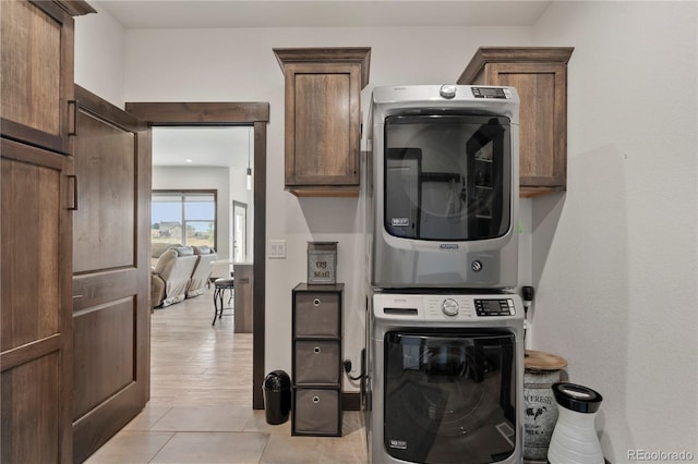 laundry room with stacked washer and dryer, light tile patterned flooring, and cabinet space