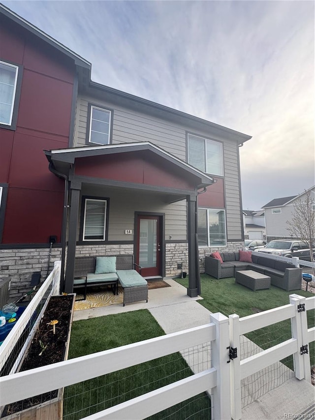 1353 Reynolds St Unit 5A, Fort Lupton, CO 80621 - view of front of property with an outdoor living space, a fenced front yard, a gate, stone siding, and covered porch