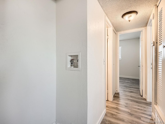 corridor with a textured ceiling and light hardwood / wood-style flooring