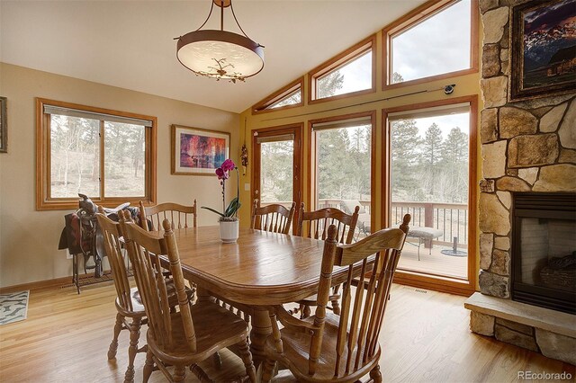 199 Elk Horn Ct, Bailey, CO 80421 - dining space featuring light wood-style flooring, plenty of natural light, vaulted ceiling, a stone fireplace, and baseboards
