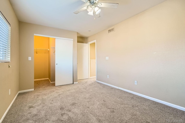 unfurnished bedroom featuring ceiling fan, a walk in closet, light carpet, and a closet