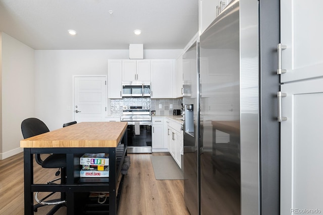 kitchen featuring appliances with stainless steel finishes, hardwood / wood-style floors, wood counters, white cabinetry, and backsplash