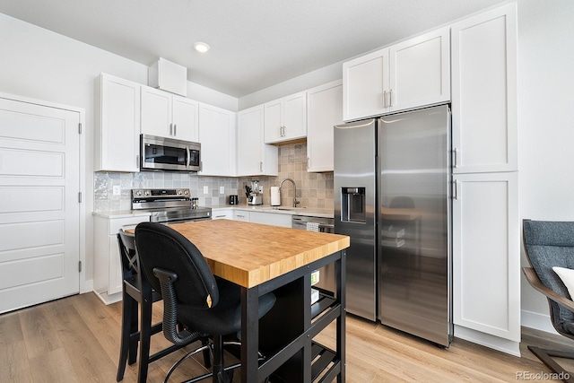 kitchen with appliances with stainless steel finishes, sink, white cabinets, and light wood-type flooring