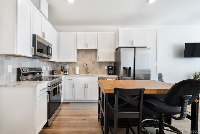 kitchen featuring sink, white cabinetry, light hardwood / wood-style flooring, stainless steel appliances, and decorative backsplash