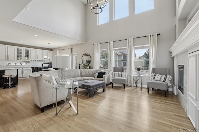 living room featuring a towering ceiling, light wood-type flooring, a chandelier, and a glass covered fireplace