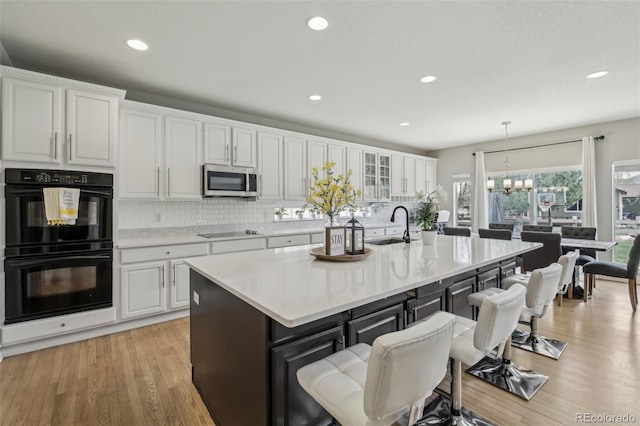 kitchen with black appliances, a sink, white cabinetry, a kitchen breakfast bar, and backsplash