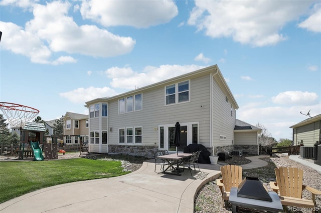 rear view of property featuring stone siding, a patio area, a playground, and cooling unit