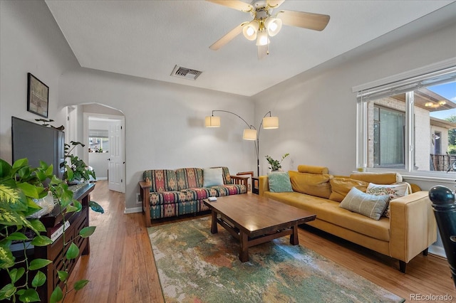 living room featuring arched walkways, visible vents, ceiling fan, wood finished floors, and baseboards