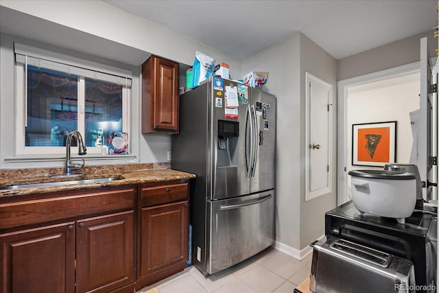 kitchen with stone counters, light tile patterned floors, stainless steel fridge with ice dispenser, a sink, and baseboards