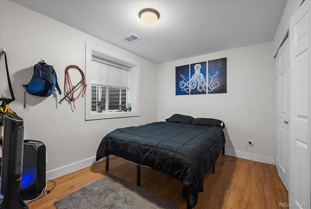 bedroom featuring a textured ceiling, wood finished floors, visible vents, and baseboards