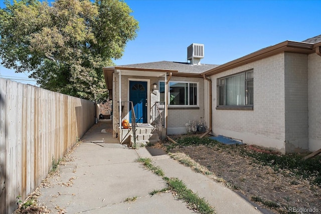 property entrance featuring fence, cooling unit, and brick siding