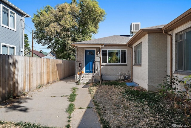 property entrance featuring brick siding, fence, and central air condition unit