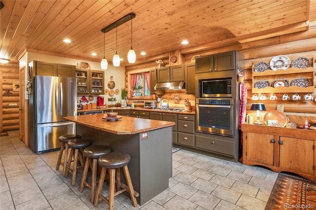 2255 Spruce Rd, Woodland Park, CO 80863 - kitchen with stainless steel appliances, log walls, under cabinet range hood, wooden ceiling, and light tile patterned floors