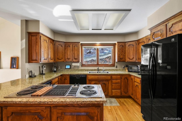 kitchen with kitchen peninsula, light stone countertops, light wood-type flooring, sink, and black appliances