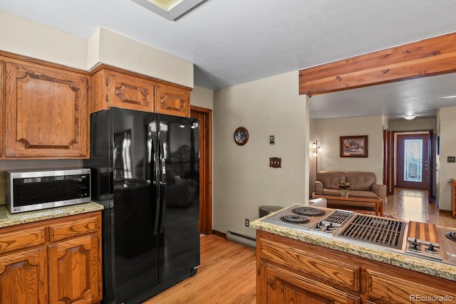 kitchen featuring light stone countertops, light wood-type flooring, baseboard heating, and appliances with stainless steel finishes