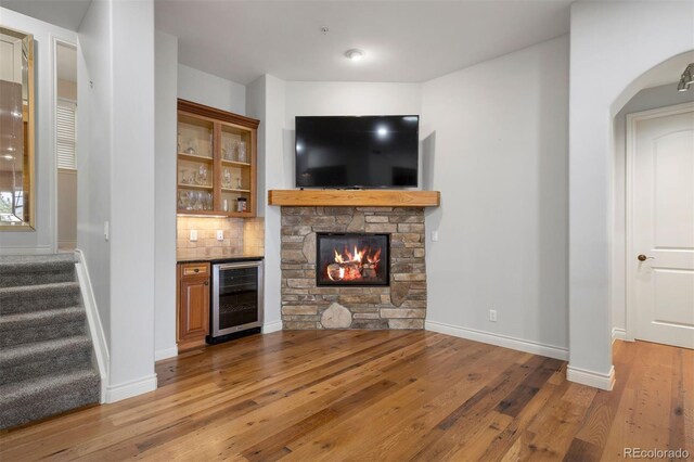 4364 Chateau Ridge Ln, Castle Rock, CO 80108 - unfurnished living room with beverage cooler, light wood-style floors, stairway, bar area, and a stone fireplace