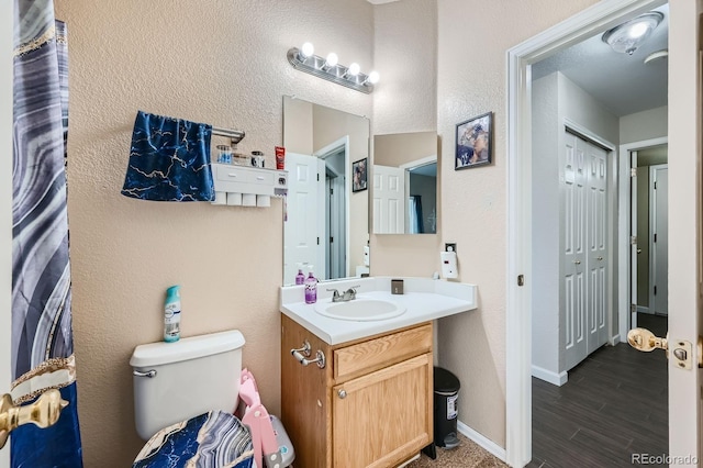 bathroom with a textured wall, toilet, wood finished floors, vanity, and baseboards