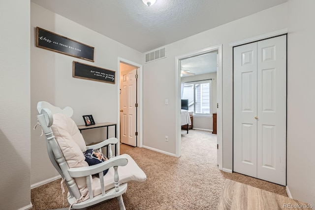 sitting room with visible vents, light carpet, baseboards, and a textured ceiling