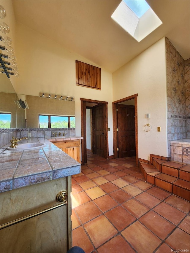 kitchen with tile counters, high vaulted ceiling, a skylight, light tile patterned floors, and sink