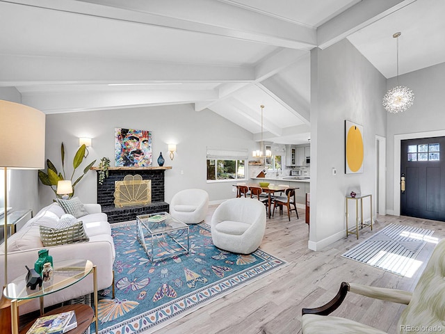 living room with a notable chandelier, light hardwood / wood-style flooring, vaulted ceiling with beams, and a fireplace