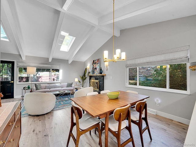 dining room with light hardwood / wood-style floors, a notable chandelier, a brick fireplace, and lofted ceiling with skylight