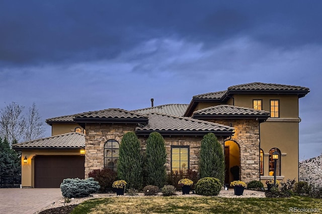 mediterranean / spanish house featuring a garage, driveway, stone siding, and stucco siding