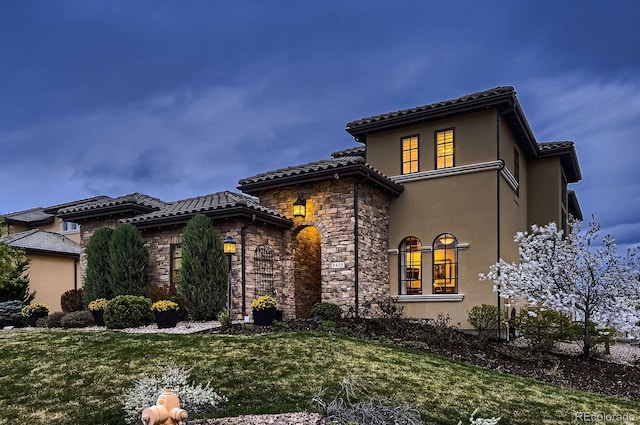 mediterranean / spanish-style house with stucco siding, a tile roof, stone siding, and a front lawn