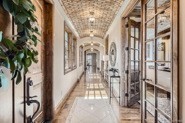 hallway featuring vaulted ceiling, brick ceiling, arched walkways, baseboards, and visible vents