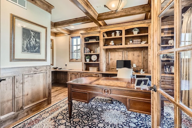 home office featuring a wainscoted wall, light wood finished floors, coffered ceiling, beam ceiling, and visible vents