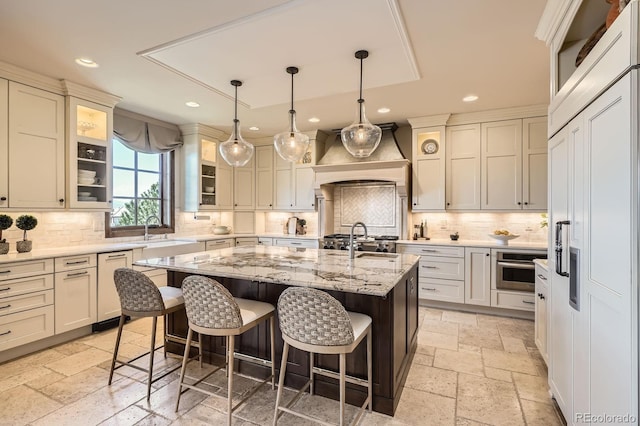 kitchen featuring a kitchen island with sink, a kitchen breakfast bar, a sink, stone tile floors, and recessed lighting