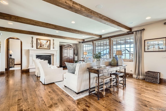 living area featuring wood finished floors, baseboards, arched walkways, and a fireplace with raised hearth