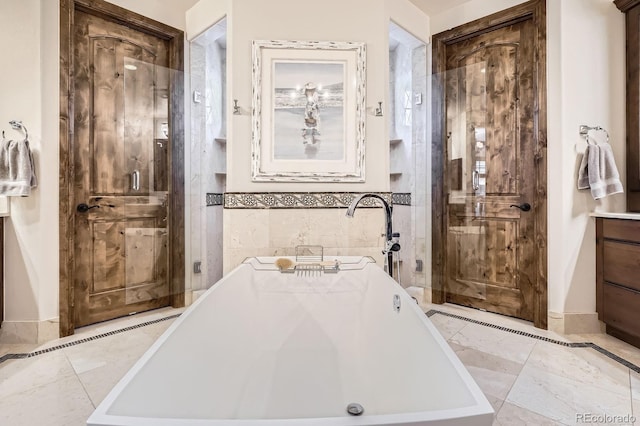 bathroom with a soaking tub, tile walls, baseboards, marble finish floor, and vanity