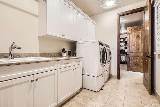 washroom with light tile patterned floors, washing machine and dryer, a sink, baseboards, and cabinet space
