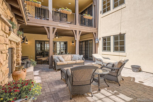 view of patio / terrace with an outdoor living space with a fireplace, a ceiling fan, and a balcony