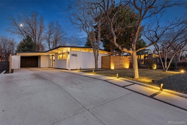 mid-century inspired home with an attached garage, concrete driveway, and fence